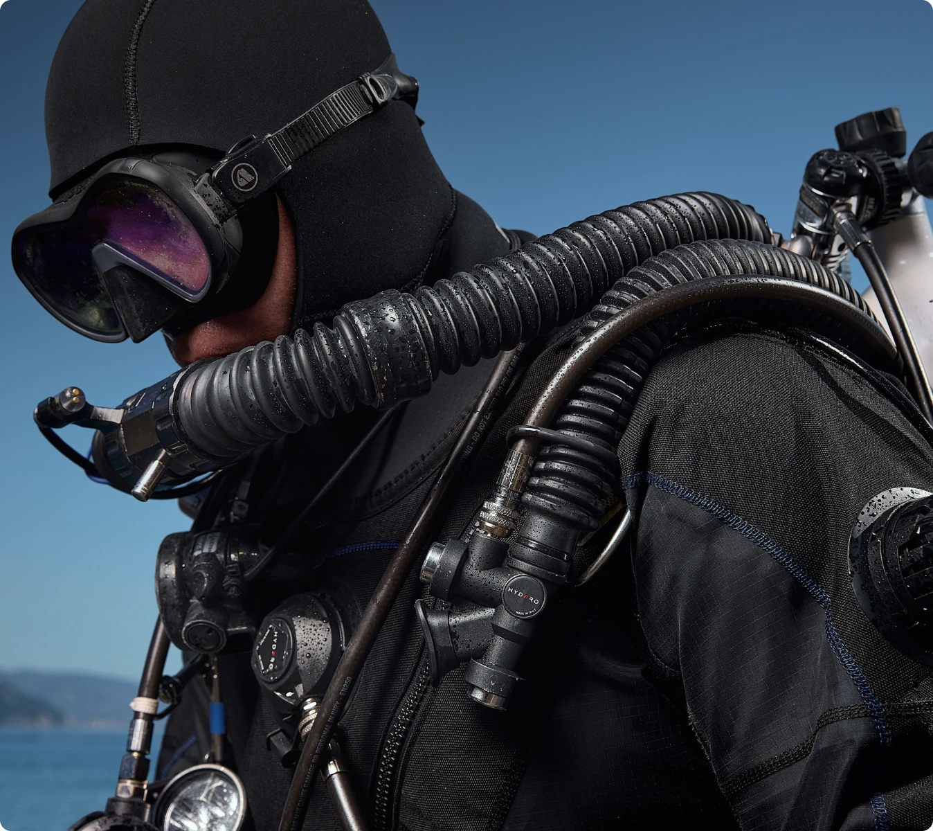 Diver in drysuit and hood breathing from the regulator at the surface, HYDPRO inflator and corrugated hose on the shoulder